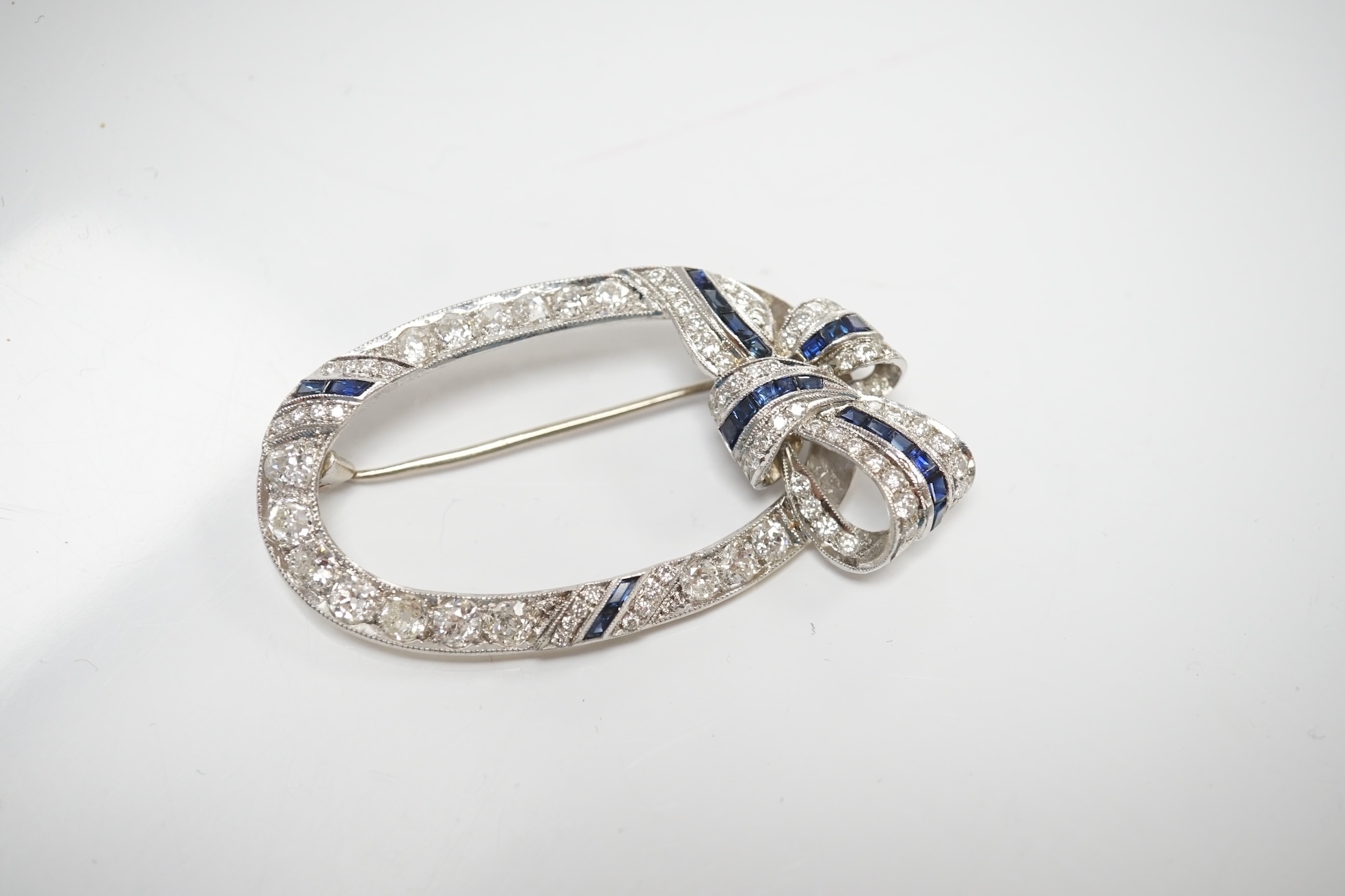 A yellow and white metal, sapphire and millegrain set diamond cluster oval open work brooch, with ribbon bow motif, 50mm, gross weight 11 grams. Condition - good